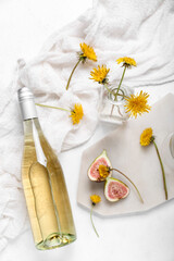 Board with bottle and glass of dandelion wine on white background