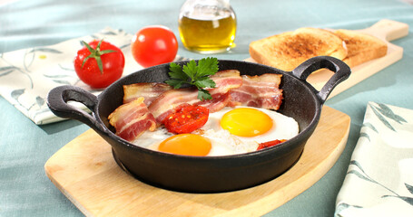 fried eggs with bacon and tomatoes in a frying pan. breakfast on the table. sunny morning. country style. organic farm food