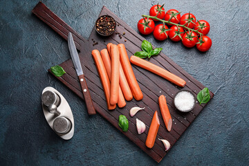 Board of tasty sausages with basil and tomatoes on dark background