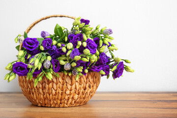 Basket with eustoma flowers on wooden table near white wall