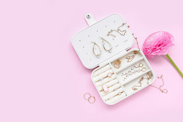 Opened organizer with stylish jewelry and flower on pink background