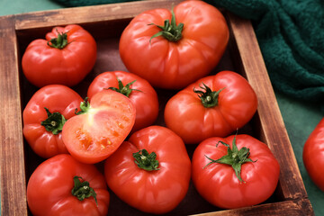Wooden box with fresh tomatoes on green background
