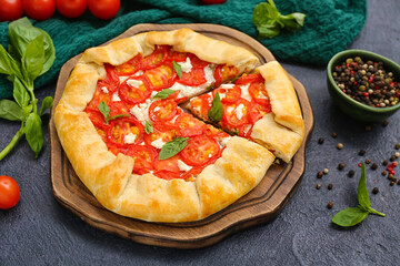 Board with tasty tomato galette and basil on dark background
