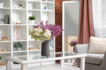 Fototapeta na wymiar Vase with beautiful lilac flowers on coffee table in interior of living room