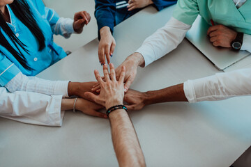 A group of doctors and a medical nurse join their hands together on a table, showcasing the...