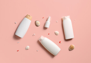 Different bottles of sunscreen cream with seashells on pink background