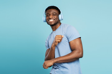 Smiling Nigerian man wearing wireless headphones listening music isolated on blue background