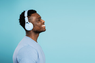 Side view african american man wearing headphones listening to music isolated on blue background