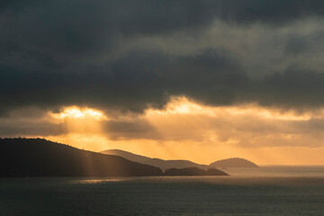 A tropical landscape with the sun breaking through clouds onto the ocean at Hamilton Island,...