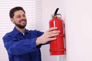 Man checking fire extinguisher indoors, selective focus - obrazy, fototapety, plakaty
