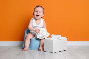 Little child sitting on baby potty and box of diapers near orange wall - obrazy, fototapety, plakaty