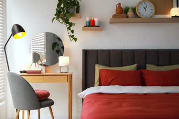 Stylish bedroom interior with comfortable bed, dressing table, lamps and green houseplant