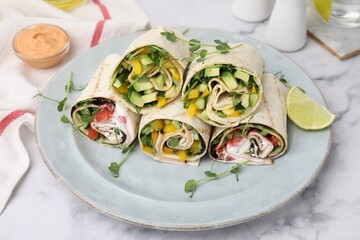 Delicious sandwich wraps with fresh vegetables and slice of lime on white marble table