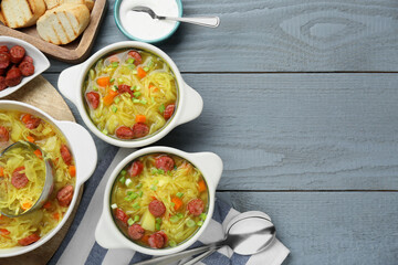 Delicious sauerkraut soup with smoked sausages and green onion served on grey wooden table, flat lay. Space for text