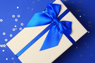 Beautiful gift box with bow and confetti on blue background, top view