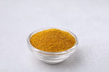 Glass bowl with curry powder on white table, closeup