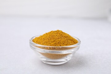 Glass bowl with curry powder on white table, closeup