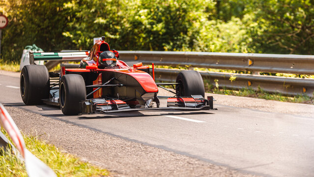 A red extreme sport car, formula 2, going fast in a European hill climb championship in Asturias, Spain, in the middle of a forest and the mountains in a sunny daylight