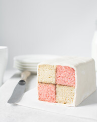 Battenburg cake on a white tray, almond and strawberry sponge cake covered in white fondant, pink and yellow check cake