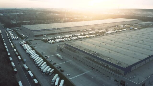 Aerial view of a large logistics park with many semi-truck with cargo trailers waiting to be unloaded and loaded at the warehouses ramps