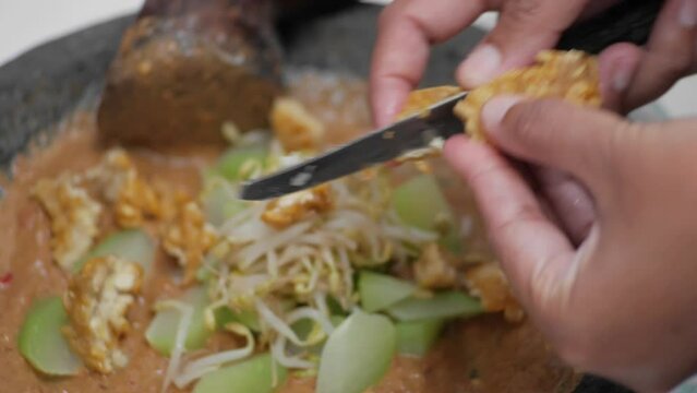 Mixing rujak seasoning that has been pulverized with various vegetables such as bean sprouts, chayote, fried tofu cucumber and fried tempeh