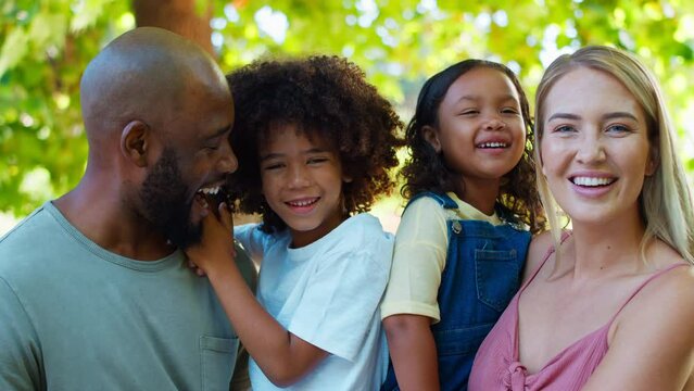 Portrait of multi-racial family standing outside in garden, park or countryside looking at camera- shot in slow motion