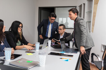 coworkers discussing company matters in a meeting room, using notebooks, laptop computer, and electronic devices, hispanic office group teamwork
