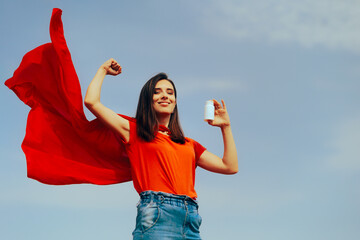 Strong Superhero Girl Holding a Bottle of Pills Feeling Strong. Happy woman flexing her muscles...