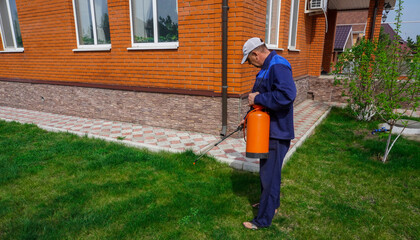 A man works in the garden, spraying weeds from a sprayer.