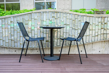 Black metal café table and chair set on a wood deck, block glass wall in background
