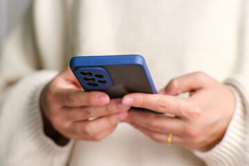 Closeup of female hand holding smartphone checking social media, playing games, online shopping relaxing on sofa. Lifestyle, free time and relaxation.