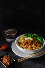 Mie ayam, noodles with chicken and vegetables in white bowl, Indonesian traditional food in dark and texture background. served with fried onions and a cup of coffee