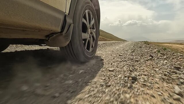 Close-up of a car driving down a dirt, rocky road, creating dust. View of the right front wheel of an SUV car in motion. Traveling by car in Kyrgyzstan. An exciting road trip.