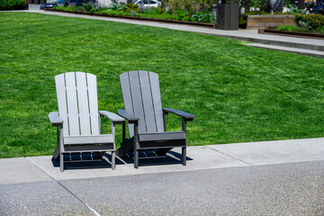 Two traditional gray Adirondack on a cement patio with vibrant green lawn in background
