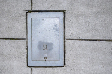 Metal cover to a small equipment vault built into a cement sidewalk
