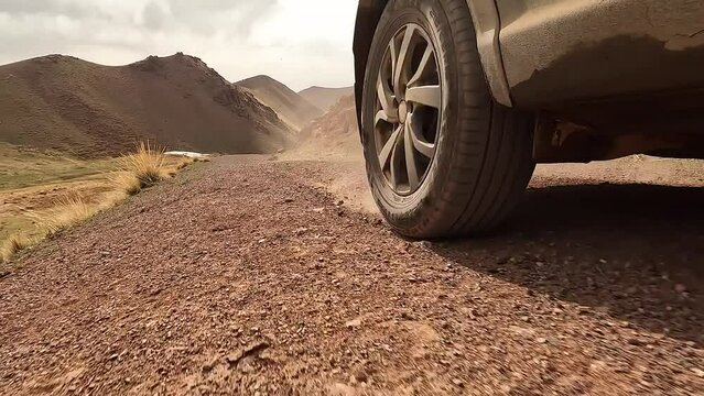 Close-up of a car driving on a dirt rocky road, creating dust. View of the right rear wheel of an SUV in motion. Traveling by car in Kyrgyzstan. An exciting road adventure.