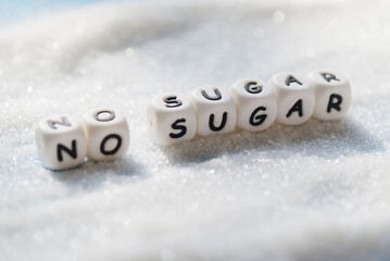 no sugar text blocks with white sugar on wooden background, suggesting dieting and eat less sugar...