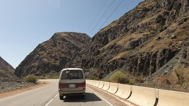 An exciting road adventure in Kyrgyzstan. Rear view of a minivan driving along a beautiful mountain road. View of the hills, rocks and mountain river. Traveling by car.