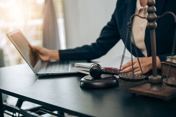 Beautiful young woman lawyer sitting in front of laptop in room with documents and smartphone with empty hammer and scale next to it justice and legal concept