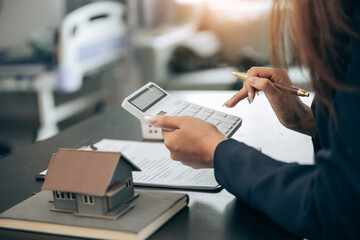 Young beautiful Asian real estate agent uses a small calculator and house models to present and advise clients on buying and selling home designs. real estate business ideas