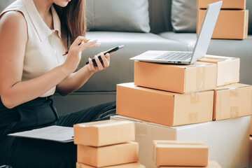 Startup Successful Small Business Owner Young Asian woman sits with laptop, calculator, smartphone and box in home preparing to ship to customer, seller business concept for SME entrepreneurs