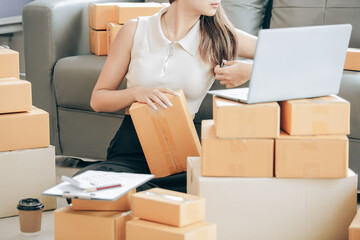 Startup Successful Small Business Owner Young Asian woman sits with laptop, calculator, smartphone and box in home preparing to ship to customer, seller business concept for SME entrepreneurs
