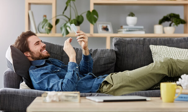 Social networking, man with smartphone on sofa and lying in living room at his home. Connectivity or technology, smile and happy male person with cellphone comfortable on couch playing online game