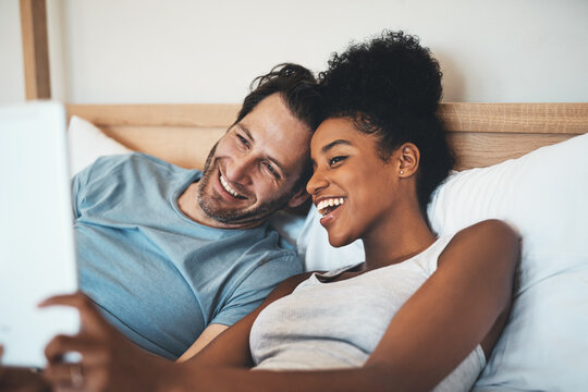 Happy interracial couple, relax and bed for selfie, photo or social media post together at home. Man and woman person with smile for fun profile picture, morning or online vlog in bedroom at a house