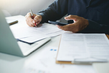 Asian businessman using a smartphone and working with  laptop while sitting at desk, Lawyer review contract, document of insurance in office