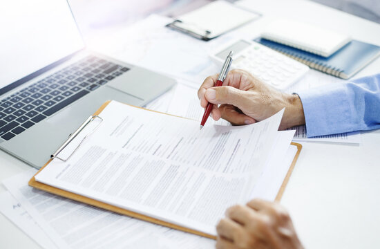 Asian businessman reviewing document reports at office workplace with computer laptop. legal expert, professional lawyer reading and checking financial documents or insurance contract