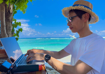 Fototapeta premium Asian man Nomad digital with laptop and running remotely with bright scenic view near poolside on the beach in summer time