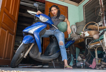Plakat A young woman is standing by a motorcycle parked in front of the entrance to a house