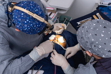 A cosmetic surgeon uses a nasal retractor to hold back a flap of skin tissue while cutting with a...