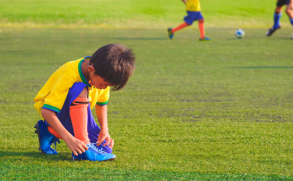 Asian little Boy in Brazilian National Football Team Uniform is tying shoelace on soccer Field during training